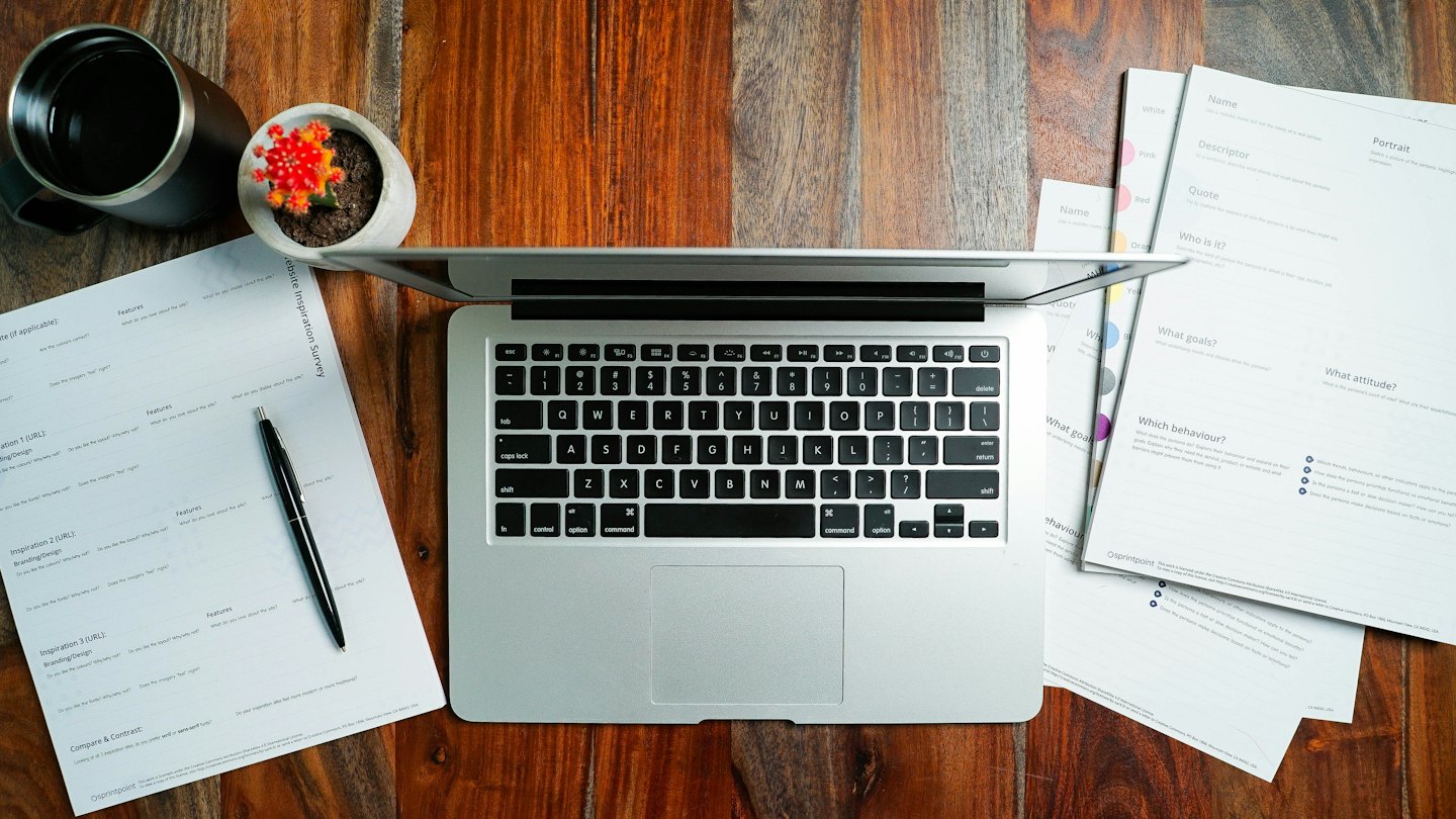 Computer portatile, documenti di sondaggio e penna su una scrivania di legno.